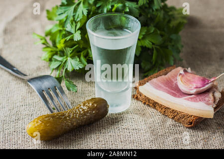 Concombre mariné sur une fourchette, un verre de vodka, de tranches de gras sur un conseil - snack-Ukrainien Banque D'Images