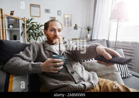 Portrait d'homme barbu d'âge moyen de regarder la télévision à la maison et de commutation satellite via la télécommande tout en vous relaxant sur le canapé confortable Banque D'Images