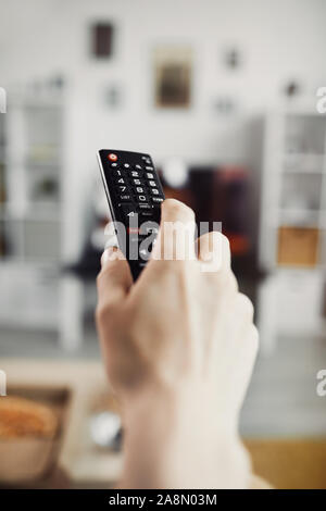 Close up of male hand holding TV remote contre grand écran de télévision, copy space Banque D'Images