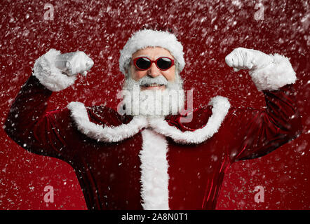 Taille portrait de funky Santa portant des lunettes de soleil et smiling at camera prêt à profiter de fête de Noël dans la neige Banque D'Images