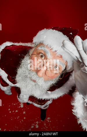 Voir ci-dessus de portrait du père Noël classique à la caméra jusqu'à en étant debout sur fond rouge dans le studio Banque D'Images
