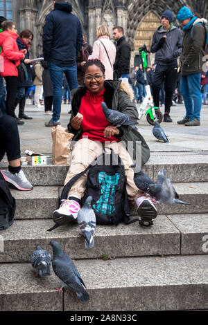 Jeune femme nourrir pigeons sauvages en face de la cathédrale, Cologne, Allemagne. junge Frau fuettert Stadttauben vor dem Dom, Köln, Deutschland. Banque D'Images