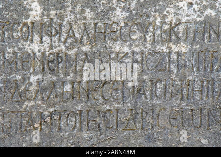 Demi-effacées le grec ancien lettres en relief sur une ancienne dalle de marbre gris et couvert avec des fissures et des moisissures. Banque D'Images