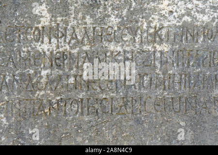 Demi-effacées le grec ancien lettres en relief sur une ancienne dalle de marbre gris et couvert avec des fissures et des moisissures. Banque D'Images