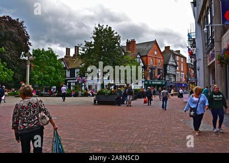 Shoppers promenade le long de la place centrale de la ville anglaise historique de Nantwich avec de jolies fleurs et d'arbres. Zone piétonne. Banque D'Images