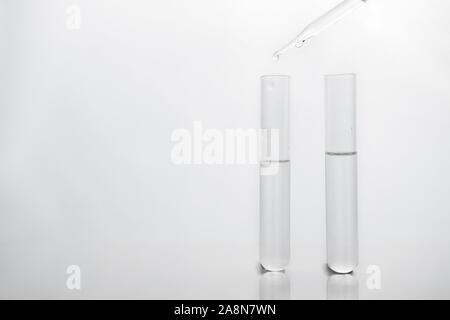 Deux tubes à essai en verre avec pipette goutte d'eau de la biotechnologie blanche sur fond propre laboratoire scientifique. Banque D'Images