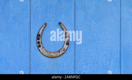 Fer à repasser ancien fer à cheval chanceux avec des clous, s'achève point jusqu'à attraper la chance, un talisman protecteur, sur une ancienne porte en bois bleu avec de la peinture craquelée Banque D'Images