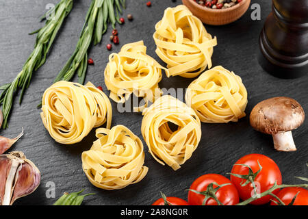 Tagliatelli spaghetti italien brut sur une plaque en ardoise noire avec légumes et épices. Banque D'Images