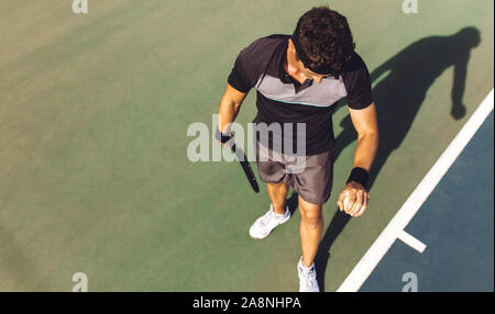 Vue de dessus du jeune homme jouant au tennis la balle qui rebondit sur le disque pour le servir. Tennis player a propos de servir le ballon dans un match. Banque D'Images
