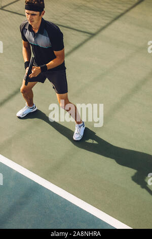 High angle shot d'un joueur de tennis jouer au tennis sur hardcourt. Jeune homme dans le sportswear debout sur la ligne de base de tennis prête à retourner le Banque D'Images