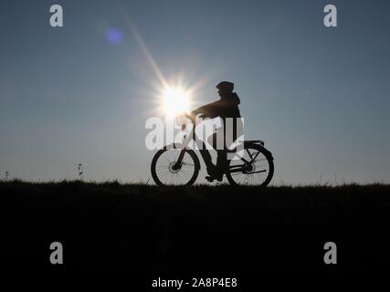 10 novembre 2019, en Rhénanie du Nord-Westphalie, Bislich : A woman rides son vélo sur la digue du Rhin dans le soleil couchant. Photo : Martin Gerten/dpa Banque D'Images