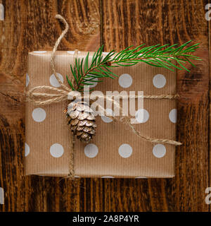 Boîte-cadeau enveloppé dans du papier craft avec le sapin et l'cône sur fond de bois rustique. Vacances de Noël concept. Image carré Banque D'Images