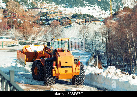 Un bulldozer avec des chaînes sur roues enlève la neige dans un village dans les montagnes d'Andorre. Banque D'Images