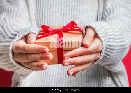 Female hands holding gift box with red ribbon close-up. Banque D'Images