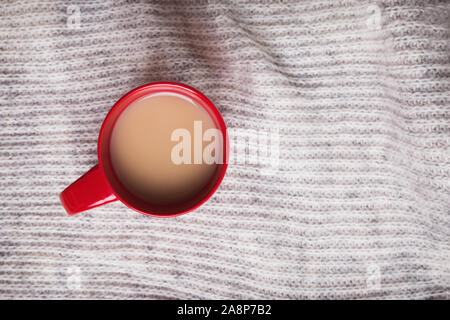 Café ou thé au lait dans la tasse rouge sur fond de tissu de laine Banque D'Images