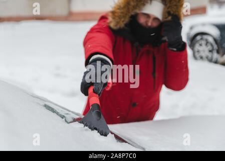 L'homme en rouge avec capuche fourrure manteau d'hiver voiture nettoyage après la tempête de neige Banque D'Images