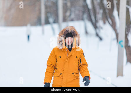 L'homme en jaune avec capuche manteau d'hiver à pied par le parc de neige Banque D'Images