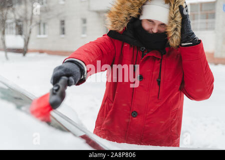 L'homme en rouge avec capuche fourrure manteau d'hiver voiture nettoyage après la tempête de neige Banque D'Images