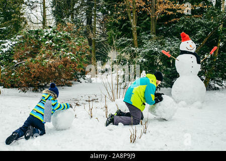 Père avec peu de fils de croisière snowman dans city park Banque D'Images