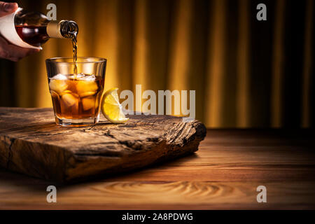 Verser dans un verre à whisky avec de la glace. Un verre de boisson alcoolisée à une table en bois avec une tranche de citron. Banque D'Images