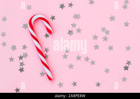 Sweet Candy Cane sur un fond rose pastel avec silver stars. Mise à plat de fête pour Noël et Nouvel An carte de vœux. Copier l'espace. Banque D'Images