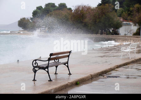 Des bancs vides par la mer agitée éclaboussé par les vagues en Dalmatie ville balnéaire en hors saison au cours de Vent du sud fort Banque D'Images