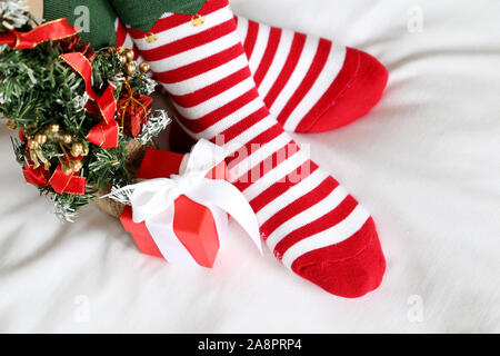 Fête de Noël à la maison, traverse les pieds en chaussettes rayées rouge et blanc et Nouvel An des arbres sur un lit. Woman in Santa vêtements et décoration de fête Banque D'Images