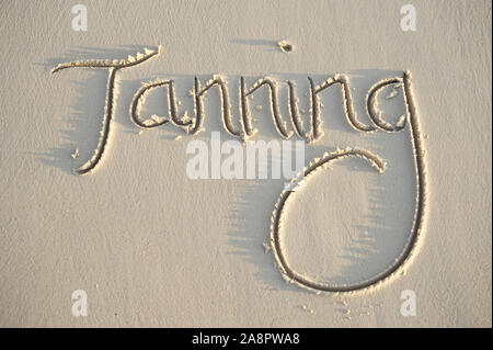 Message de bronzage manuscrit en lettres texturées dans du sable lisse Banque D'Images