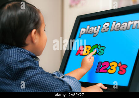 Un petit enfant regardant un écran tactile et à l'aide de l'index d'apprendre sa ABC et chiffres. Banque D'Images