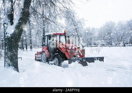 Un vieux tracteur rouge efface la rue de la neige dans une tempête de neige. Le nettoyage des rues en hiver. Banque D'Images