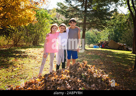 Trois jeunes amis à l'extérieur par des tas de feuilles Banque D'Images