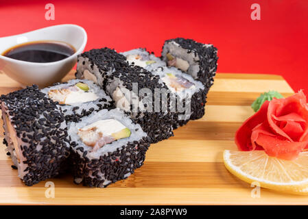 Sushi, rouleaux de sésame noir, avec du fromage, de la crevette et du crabe. Sur la planche. Sur un fond rouge. Banque D'Images