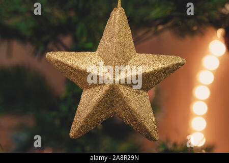 Photo d'une étoile d'or ornement de Noël sur un arbre de Noël. Lumière de Noël dans l'arrière-plan. Banque D'Images