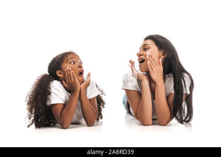 Choqué african american mother and daughter looking at each other while lying on white background Banque D'Images