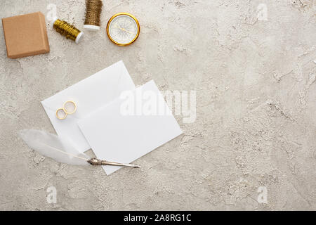 Vue de dessus les anneaux d'or blanc, près de carte vide plume, bobines, boussole et boîte-cadeau sur la surface texturée Banque D'Images