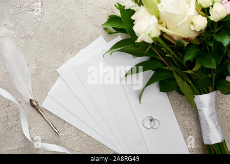 Vue du dessus de l'argent sur des enveloppes près de bouquet, ruban blanc et gris plume sur la surface texturée Banque D'Images