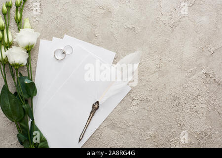 Vue du dessus de l'argent et les cartes d'invitation sur la plume d'eustoma proche du blanc des fleurs sur la surface texturée Banque D'Images