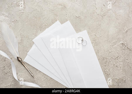 Vue du dessus de l'argent sur des enveloppes près de ruban blanc et gris plume sur la surface texturée Banque D'Images