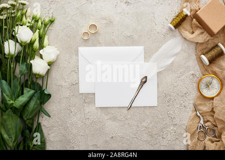 Vue de dessus sur la plume d'une carte vide, eustomia, fleurs de mariage, coffret-cadeau, compas, ciseaux et bobines sur rond des sacs sur la surface texturée Banque D'Images