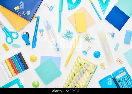 Vue de dessus bleu et jaune de fournitures scolaires dispersés avec des blocs-notes, crayons et calculator isolated on white Banque D'Images