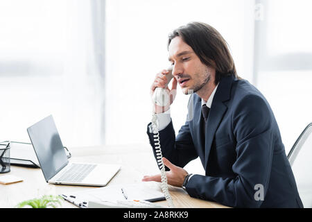 Businessman talking on phone, assis dans le bureau et à l'écart Banque D'Images
