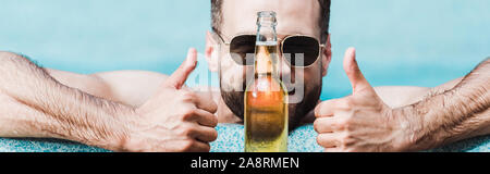 Homme barbu de lunettes en montrant Thumbs up près de bouteille avec de la bière Banque D'Images
