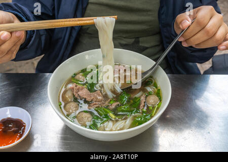 Vietnamienne à l'aide de baguettes et cuillère en mangeant des nouilles Pho Banque D'Images