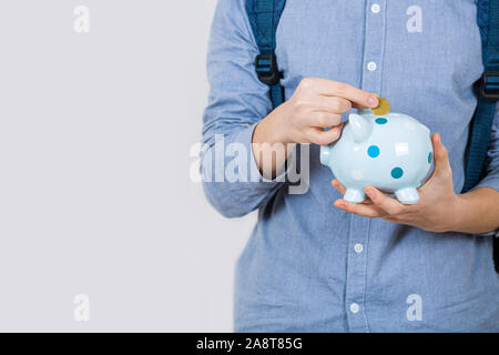 Adolescent boy holding piggy bank mettant les pièces en euros à l'intérieur sur fond blanc. L'épargne financière concept. Banque D'Images