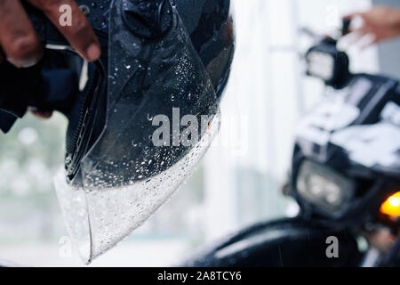 Close-up image de verre casque humide avec des gouttes d'eau dans les mains d'un motocycliste Banque D'Images