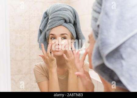 Une belle fille avec une serviette sur la tête des patchs hydrogel bâtons sous ses yeux sur son visage. La jeune fille prend soin de la peau et hydrate la zone aro Banque D'Images