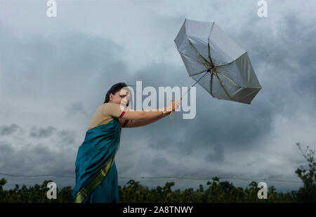 Femme essayant de tenir sur le parapluie en cas de mauvais temps Banque D'Images