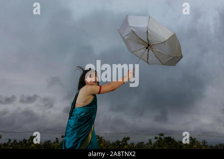 Femme essayant de tenir sur le parapluie en cas de mauvais temps Banque D'Images