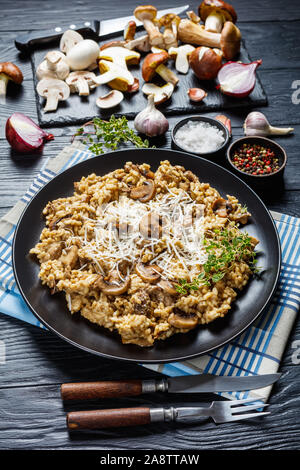 Vue verticale de champignons risotto crémeux avec du fromage râpé et le thym sur une plaque noire avec des ingrédients sur une table en bois Banque D'Images