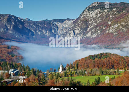 Belle vue aérienne du lac de Bohinj avec l'augmentation du brouillard, l'église de Jean le Baptiste et les montagnes environnantes sur un beau matin d'automne, la Slovénie. Banque D'Images